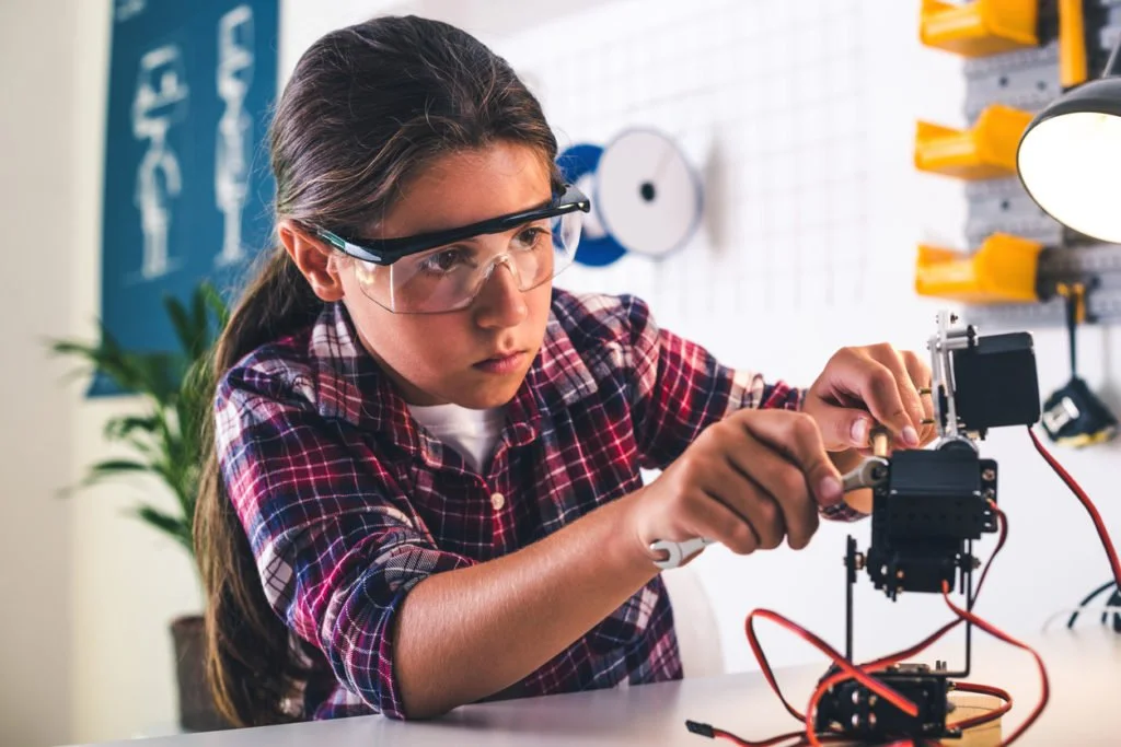 Niña en un laboratorio robótico ajustando el modelo de un brazo de robot para fomentar el interés femenino en carreras de tecnología